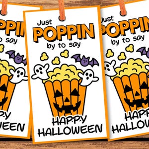 May include: Three Halloween-themed gift tags with orange popcorn bucket graphics and the text "Just Poppin by to say Happy Halloween." The tags are on a wooden surface with Halloween-themed cookies and candies.
