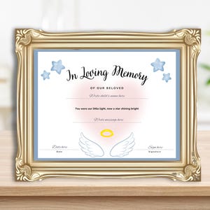 May include: A framed memorial print with a gold-colored ornate frame. The print has a light blue border and features the text "In Loving Memory" with space to write a child's name and a message. Blue star illustrations and angel wings are also included.
