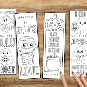 May include: Four white rectangular bookmarks with black line art and text. The bookmarks feature Halloween and religious themes, including ghosts, a mummy, a pumpkin, and Bible verses. Colored pencils are in the foreground.