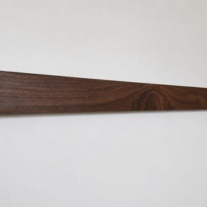 May include: A dark brown, rectangular wooden shelf mounted on a white wall. The shelf is made of solid wood, with visible grain patterns. The shelf is approximately 48 inches long and 3 inches wide.