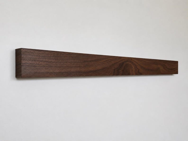 May include: A dark brown, rectangular wooden shelf mounted on a white wall. The shelf is made of solid wood, with visible grain patterns. The shelf is approximately 48 inches long and 3 inches wide.