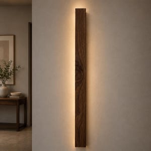 May include: A vertical, rectangular wooden wall sconce with a warm, glowing light emanating from the center. The sconce is made of dark brown wood and is mounted on a neutral-colored wall. The design is minimalist and modern.
