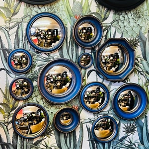 May include: A collection of 10 round blue and gold framed mirrors with various designs. The mirrors are arranged in a circular pattern on a white background with green leaves.