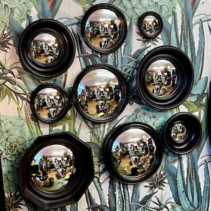 Puede incluir: Un conjunto de diez espejos redondos con marco negro y diferentes diseños. Los espejos están dispuestos en un patrón circular sobre un fondo estampado verde y blanco.