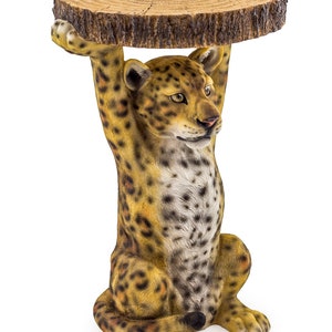 May include: A wooden table top sits on the back of a leopard figurine. The leopard is sitting on its haunches with its front paws raised. The table top is made of a natural wood slice with bark around the edges.
