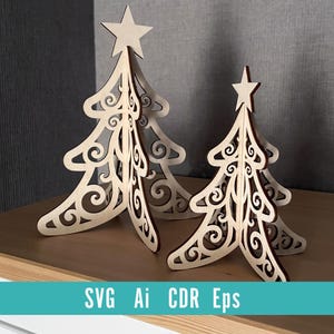 May include: Three wooden Christmas tree decorations with star toppers. The trees have a detailed, openwork design with swirling patterns. The trees are light brown and stand on a wooden surface. The text "SVG Ai CDR Eps" is at the bottom.
