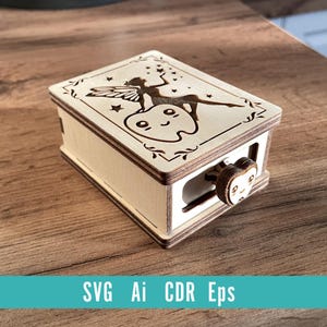May include: A wooden tooth fairy box with a laser-cut design. The box features a fairy and tooth illustration on the lid, with a decorative border. The box has a small, round knob with a face on it. The text "SVG Ai CDR Eps" is at the bottom.