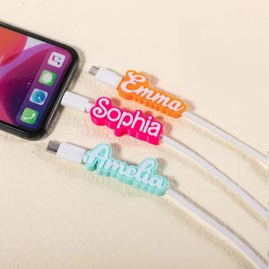 May include: Three white charging cables with colorful personalized name tags. The names are "Emma", "Sophia", and "Amelia".
