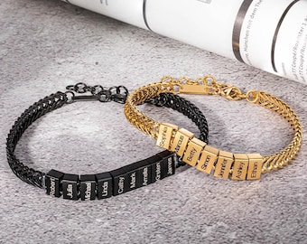 May include: Two personalized bracelets. One is black with black square beads, the other is gold with gold square beads. Each bracelet has names engraved on the beads. The bracelets are on a gray surface.