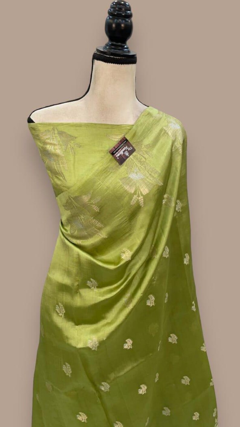 Puede incluir: Un sari de seda verde con un patr&oacute;n floral plateado. El sari est&aacute; drapeado sobre un maniqu&iacute;.
