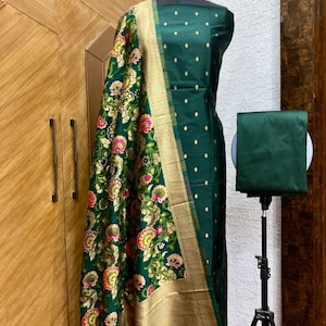May include: A green and gold Indian salwar kameez with a floral pattern. The kameez is a long, loose-fitting tunic, and the salwar is a pair of wide-legged trousers. The dupatta is a long scarf that is often worn over the head or shoulders.