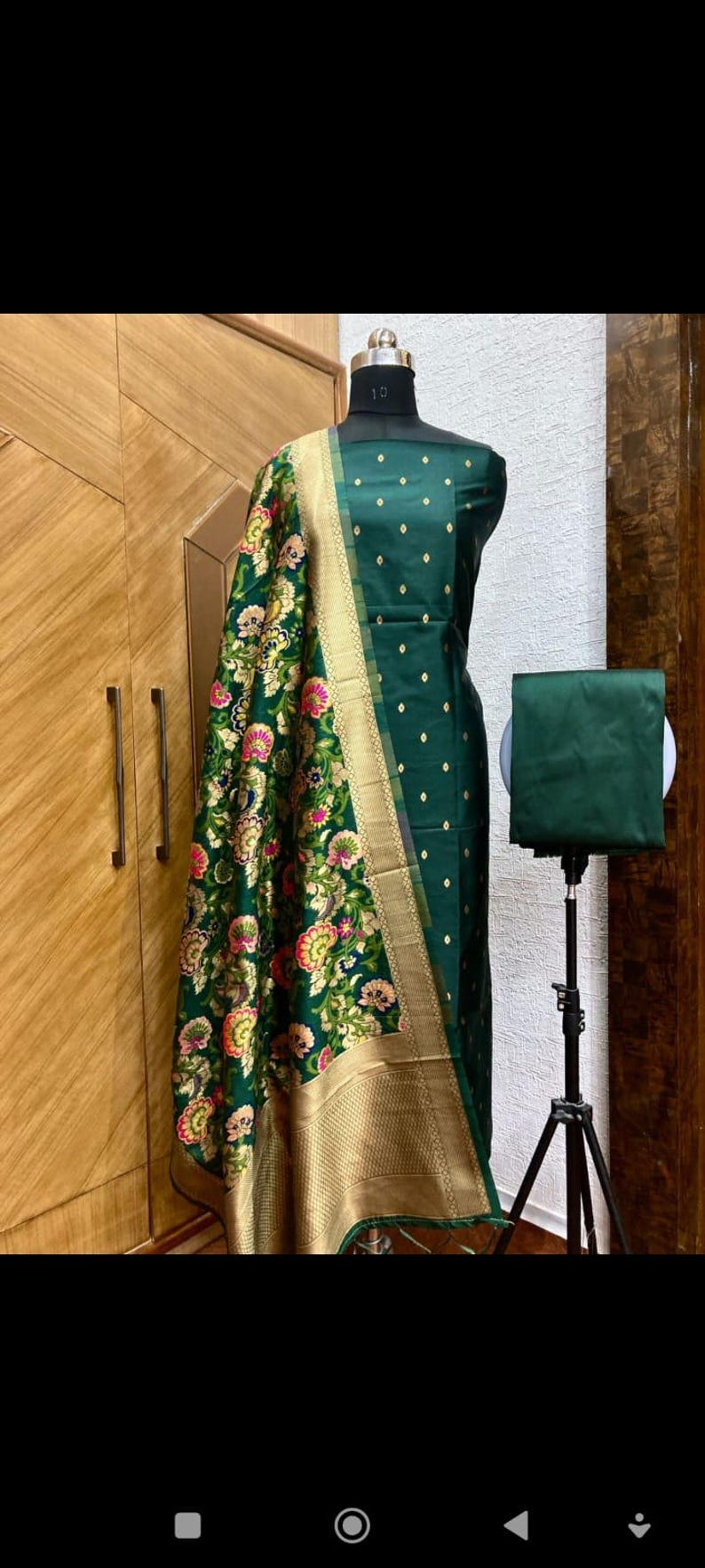 May include: A green and gold Indian salwar kameez with a floral pattern. The kameez is a long, loose-fitting tunic, and the salwar is a pair of wide-legged trousers. The dupatta is a long scarf that is often worn over the head or shoulders.