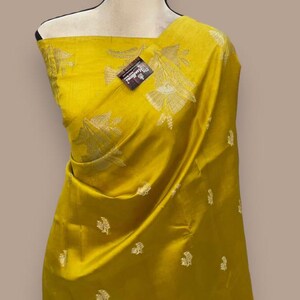 Puede incluir: Un sari de seda amarillo con un patr&oacute;n floral dorado. El sari est&aacute; drapeado en un maniqu&iacute;.