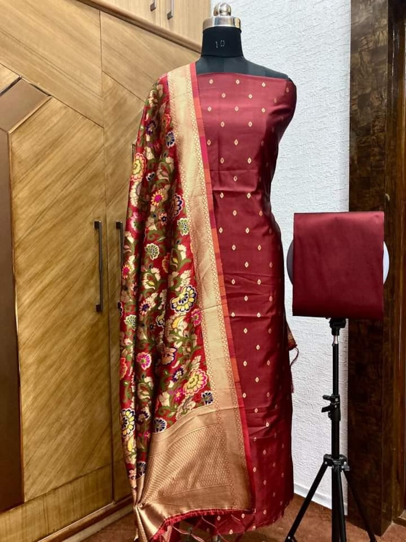 May include: A maroon dress fabric with a small diamond pattern, a maroon dupatta with a floral pattern, and a maroon plain fabric. The fabric is displayed on a mannequin.