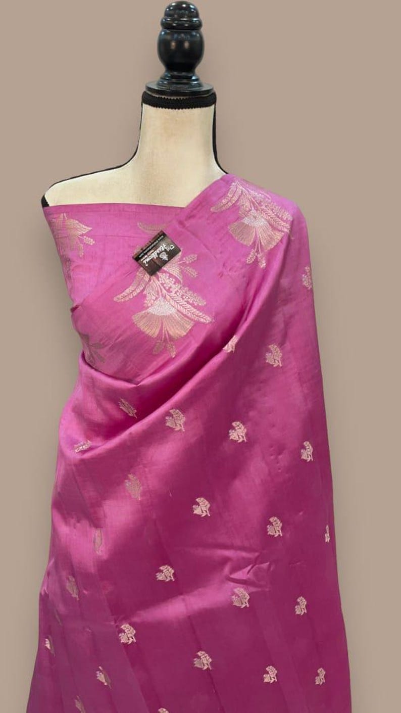 Puede incluir: Un sari de seda rosa con un patr&oacute;n floral plateado. El sari est&aacute; drapeado en un maniqu&iacute;.