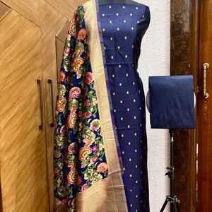 May include: A navy blue dress fabric with a gold and white floral pattern. The fabric is on a dress form and has a matching dupatta with a gold border.
