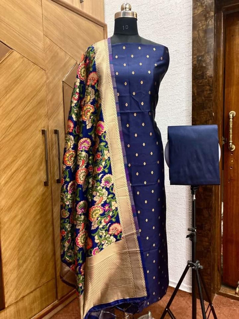 May include: A navy blue dress fabric with a gold and white floral pattern. The fabric is on a dress form and has a matching dupatta with a gold border.