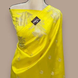 Puede incluir: Un sari de seda amarillo con un patr&oacute;n floral plateado. El sari est&aacute; drapeado sobre un maniqu&iacute;.