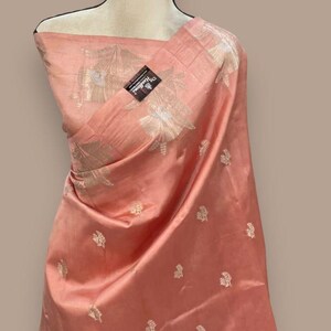 Puede incluir: Un sari de seda de color melocot&oacute;n con un patr&oacute;n floral plateado. El sari est&aacute; drapeado sobre un maniqu&iacute; blanco.