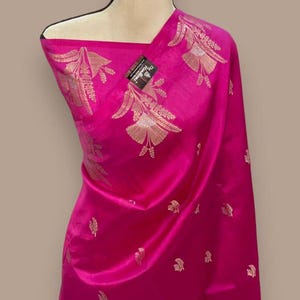 Puede incluir: Un sari de seda rosa con bordados dorados de dise&ntilde;os florales. El sari est&aacute; drapeado en un maniqu&iacute;.