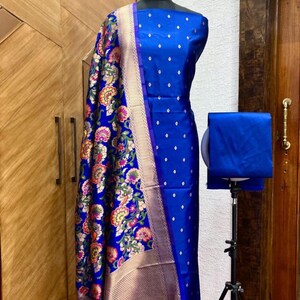 May include: A blue and gold patterned fabric with a floral design. The fabric is draped over a dress form and is accompanied by a solid blue fabric.
