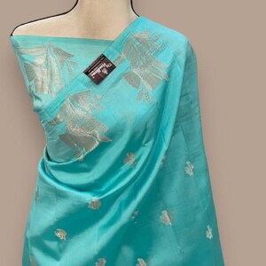 Puede incluir: Un sari de seda azul turquesa con bordados plateados. El sari tiene un dise&ntilde;o floral y est&aacute; drapeado en un maniqu&iacute;.