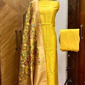May include: A yellow dress with a matching dupatta. The dupatta has a floral pattern in gold, red, and green. The dress has a dotted pattern.