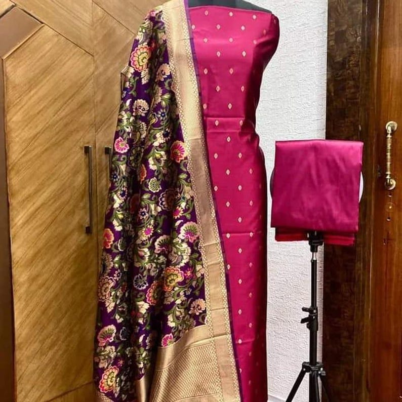 May include: A magenta and purple Indian salwar kameez suit with a floral patterned dupatta. The suit is made of silk and has a gold border.
