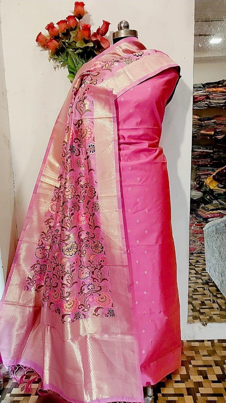 May include: A pink and gold patterned silk dupatta with a pink silk dress. The dupatta has a floral design with gold accents. The dress has a dotted pattern.