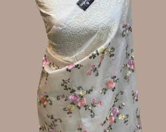 May include: A sheer white fabric with floral embroidery in shades of pink, yellow, and green. The fabric has a delicate lace trim around the edges.