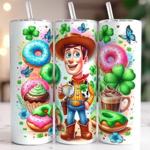 May include: A white tumbler with a green, white, and blue design featuring a cartoon character, donuts, cupcakes, and shamrocks. The character is wearing a cowboy hat and holding a cup of coffee.