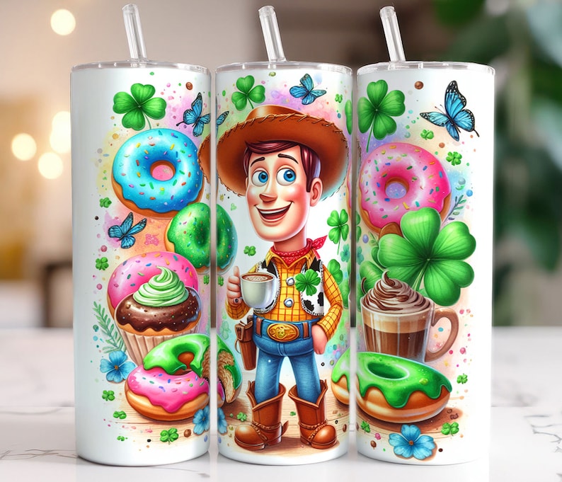 May include: A white tumbler with a green, white, and blue design featuring a cartoon character, donuts, cupcakes, and shamrocks. The character is wearing a cowboy hat and holding a cup of coffee.