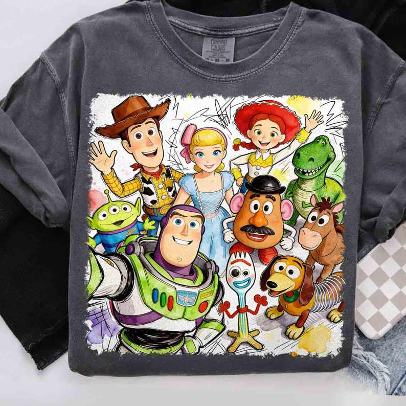 Pode incluir: Uma camiseta cinza carv&atilde;o com um gr&aacute;fico em estilo aquarela de personagens do filme Toy Story. O design inclui Woody, Buzz Lightyear, Bo Peep e outros personagens. O gr&aacute;fico &eacute; emoldurado com uma borda branca.