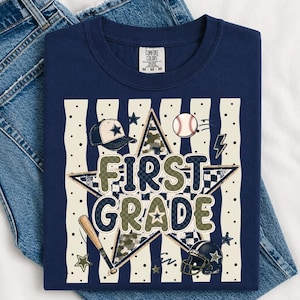 以下が含まれることがあります： FIRST GRADEという文字がプリントされたネイビーブルーのTシャツ。大きな星、野球帽、野球ボール、バット、フットボールヘルメットが描かれており、背景には黒いドットが入ったクリーム色の縦縞模様があしらわれています。