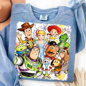 Pode incluir: Camisola azul clara com gola redonda com um gr&aacute;fico colorido de personagens do filme de anima&ccedil;&atilde;o Toy Story. O gr&aacute;fico inclui Woody, Buzz Lightyear e outros personagens amados. A camisola &eacute; feita de um material macio.