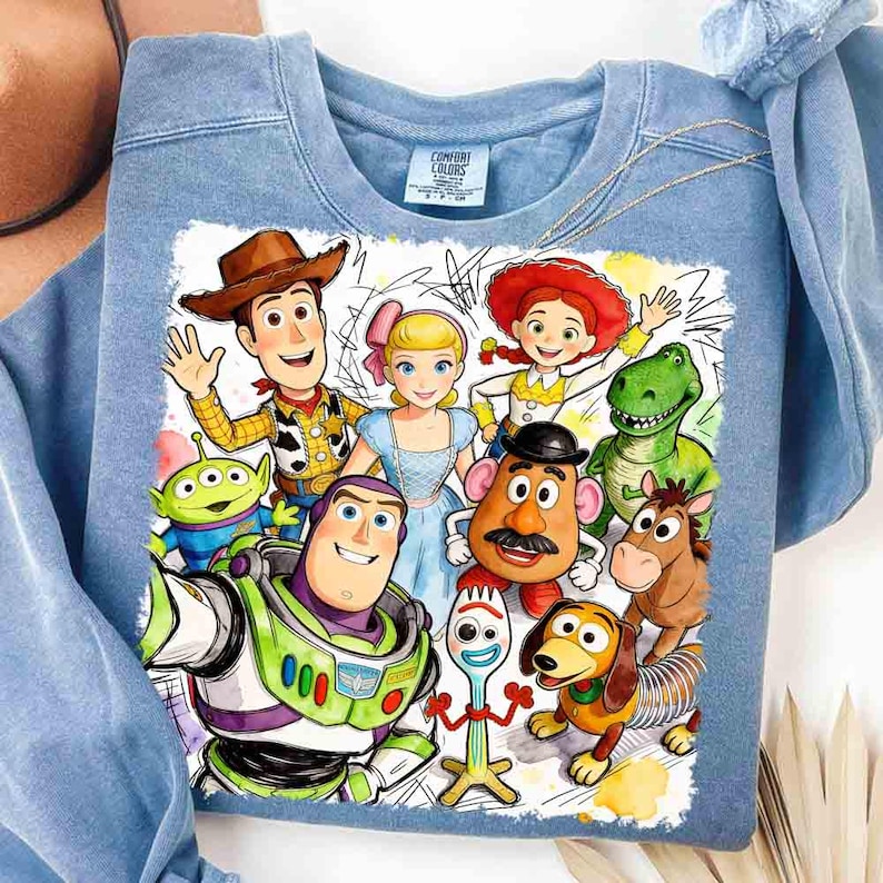 Pode incluir: Camisola azul clara com gola redonda com um gr&aacute;fico colorido de personagens do filme de anima&ccedil;&atilde;o Toy Story. O gr&aacute;fico inclui Woody, Buzz Lightyear e outros personagens amados. A camisola &eacute; feita de um material macio.