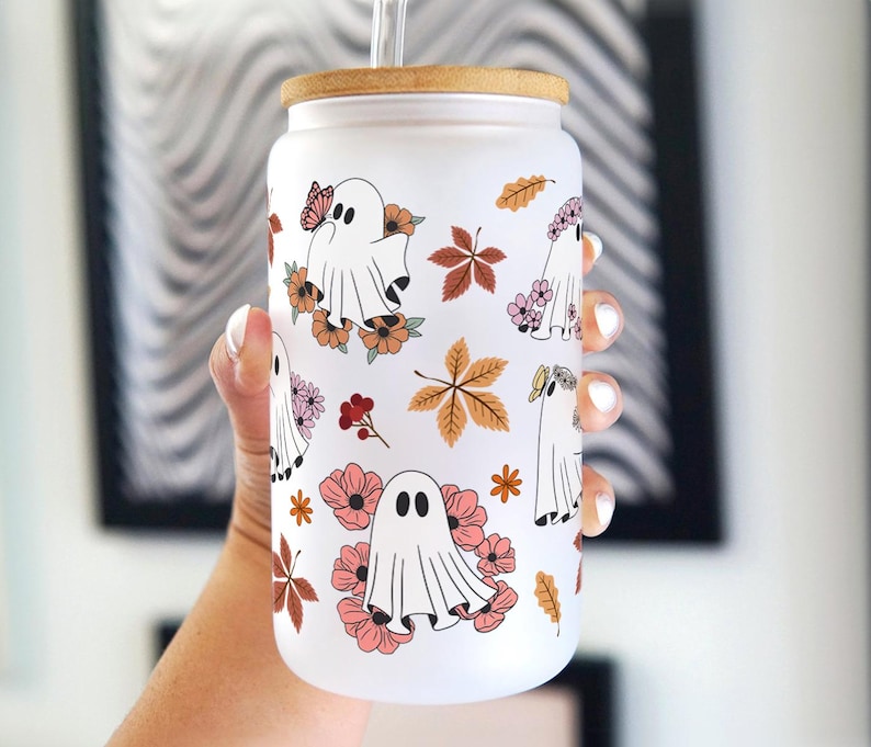 Op de afbeelding: Een witte beker met een houten deksel en een rietje. De beker heeft een patroon van geesten, bloemen en bladeren in tinten roze, oranje en bruin.