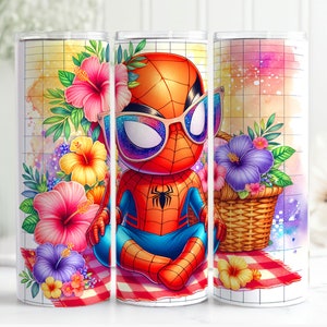 May include: A white tumbler with a red and blue cartoon superhero wearing sunglasses and sitting on a picnic blanket with flowers. The tumbler has a white background with a grid pattern.