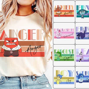 Peut inclure: Un t-shirt blanc avec un graphique rétro du personnage Colère du film Vice-Versa. Le graphique présente le visage de Colère et le mot "Colère" dans une police de caractères stylisée. Le t-shirt est un excellent moyen de montrer votre amour pour le film et le personnage.