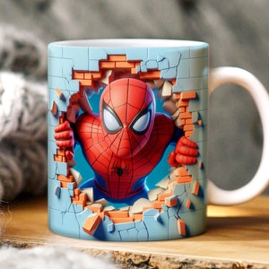 May include: A blue ceramic mug with a 3D image of Spiderman breaking through a brick wall. The mug has a white handle.