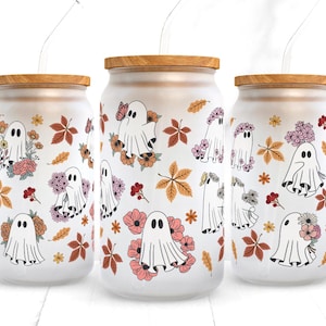 Op de afbeelding: Drie glazen potten met houten deksels en rietjes. Elke pot heeft een witte achtergrond met een patroon van geesten, bloemen en bladeren in tinten roze, oranje en geel.