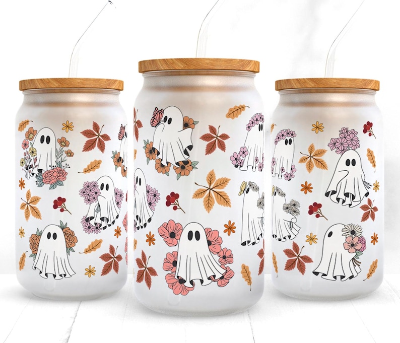 Op de afbeelding: Drie glazen potten met houten deksels en rietjes. Elke pot heeft een witte achtergrond met een patroon van geesten, bloemen en bladeren in tinten roze, oranje en geel.