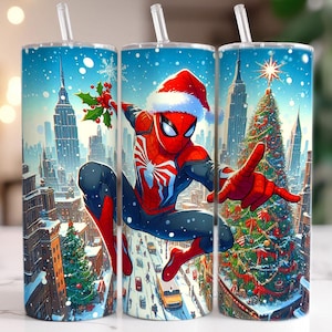 May include: Three stainless steel tumblers with a winter holiday theme. Each tumbler features a vibrant illustration of Spider-Man in a Santa hat, set against a snowy cityscape with Christmas trees and skyscrapers. The tumblers have clear straws.