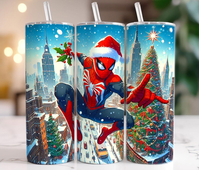 May include: Three stainless steel tumblers with a winter holiday theme. Each tumbler features a vibrant illustration of Spider-Man in a Santa hat, set against a snowy cityscape with Christmas trees and skyscrapers. The tumblers have clear straws.