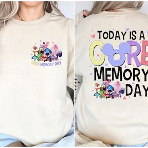 May include: A cream coloured sweatshirt with a graphic of characters from the movie Inside Out. The text "Core Memory Day" is printed below the graphic. The back of the sweatshirt has the text "Today is a Core Memory Day" with a Mickey Mouse head in the middle of the word "Core".