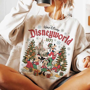 May include: A white sweatshirt with a Christmas-themed design featuring Mickey Mouse, Minnie Mouse, Goofy, Donald Duck, and a castle. The text "Walt Disney World 1971" is printed on the sweatshirt.