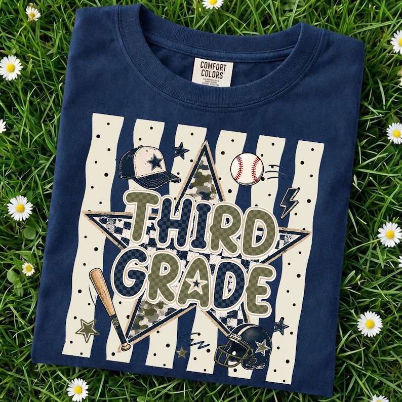 以下が含まれることがあります： 大きな文字で「THIRD GRADE」と書かれたグラフィックプリントが施されたネイビーブルーのTシャツ。中央の星、野球帽、野球ボール、バット、フットボールヘルメットが、縦縞の背景の上にデザインされています。