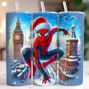 May include: Three blue insulated tumblers with white straws. Each tumbler features a winter scene with a superhero wearing a Santa hat. The background includes iconic buildings and falling snow, creating a festive holiday theme.