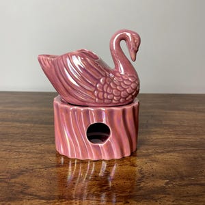 May include: A pink ceramic swan oil burner with a textured base. The swan has a detailed design and a hole in the top for a tea light.