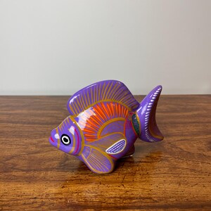 May include: Purple ceramic fish figurine with orange, yellow, and green painted details. The fish has a stylized design and is a traditional Mexican folk art piece.